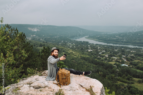 Young hiker man makes selfie on the background of the summer landscape.The guy has a long beard.Hiking and recreation theme.