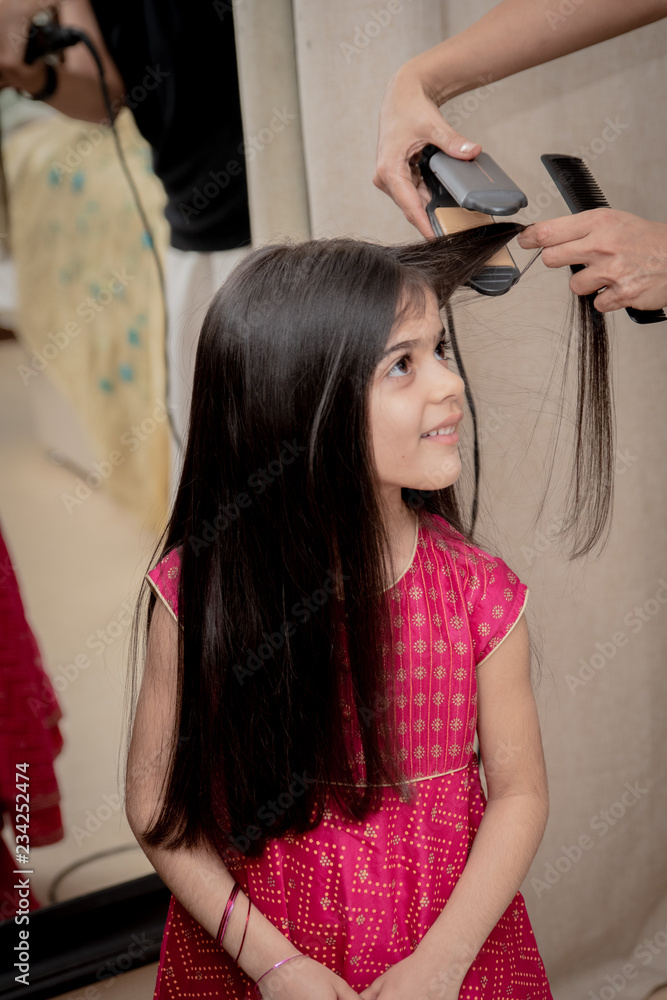 Fototapeta premium 6 year old girl has her hair straightened by her mother at home. 