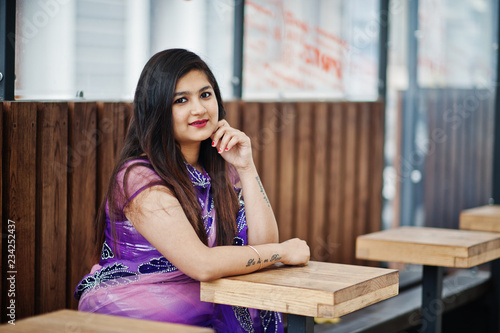 Indian hindu girl at traditional violet saree sitting at cafe table.
