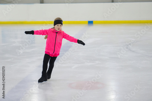 Little girl learning to ice skate. Figure skating school. Young figure skaters practicing at indoor skating rink.