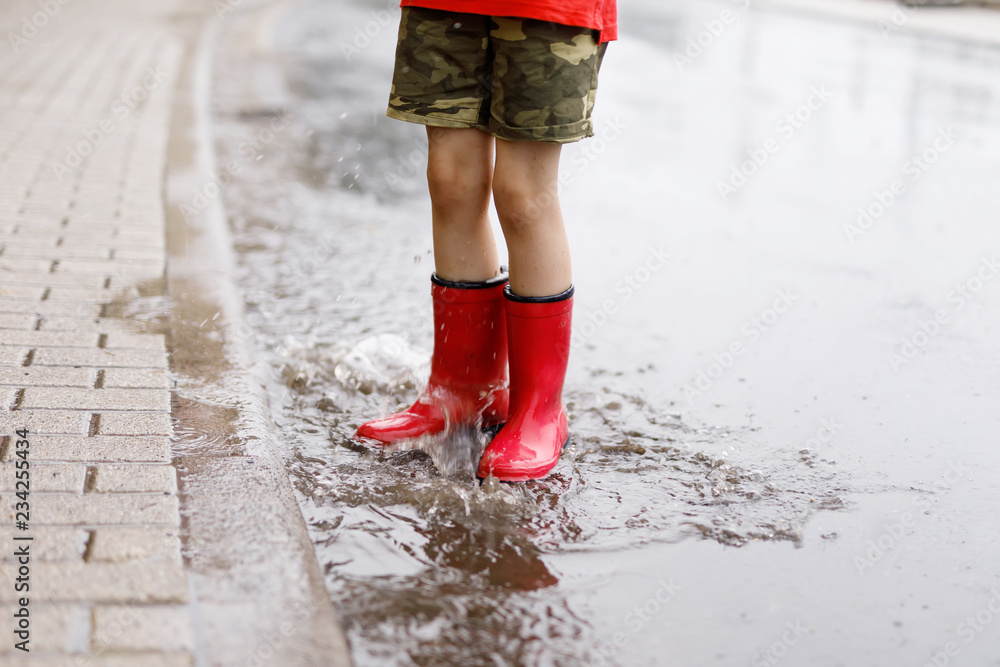 Child wearing red rain boots jumping into a puddle. Close up. Kid
