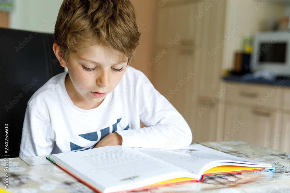 Little blonde school kid boy reading a book at home. Child interested in reading magazine for kids. Leisure for kids, building skills and education concept.. Little blonde school kid boy reading a book at home. Child interested in reading magazine for kids. Leisure for kids, building skills and education concept..