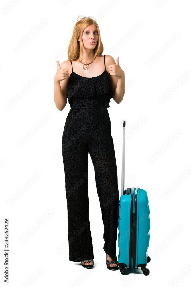 Blond girl traveling with her suitcase giving a thumbs up gesture with both hands and smiling. Cheerful expression on isolated white backgroun Blond girl traveling with her suitcase giving a thumbs up gesture with both hands and smiling. Cheerful expression on isolated white backgroun