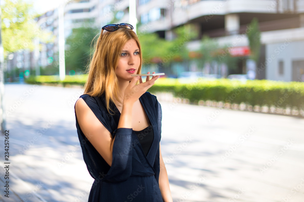 Pretty young teenager girl sending an audio by mobile at the street