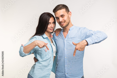 People and gesture concept - young pretty woman and handsome man pointing down over white background