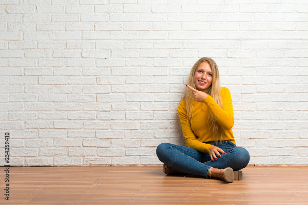Young girl sitting on the floor pointing to the side with a finger to present a product Young girl sitting on the floor pointing to the side with a finger to present a product