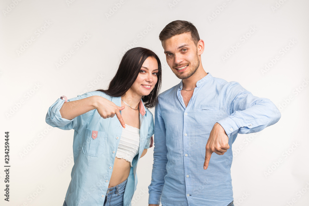 People and gesture concept - young pretty woman and handsome man pointing down over white background People and gesture concept - young pretty woman and handsome man pointing down over white background
