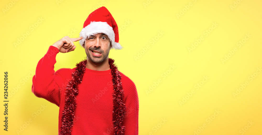 Man with red clothes celebrating the Christmas holidays making the gesture of madness putting finger on the head on yellow background Man with red clothes celebrating the Christmas holidays making the gesture of madness putting finger on the head on yellow background
