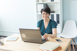 Business, technology and people concept - middle aged woman at work using a laptop and smile