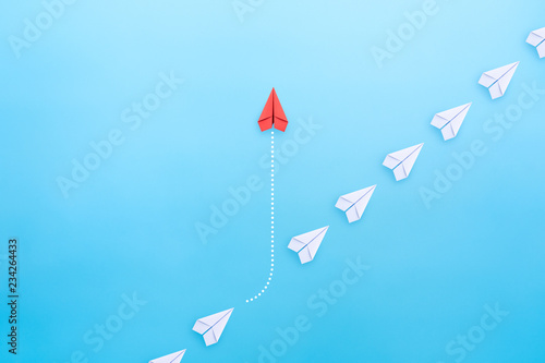 Business concept for innovation and solution with group of white paper plane in one direction and one red paper plane pointing in different way on blue background.