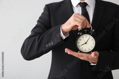 Businessman with alarm clock on light background, closeup