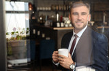 Handsome businessman drinking coffee in cafe, view through window from outside
