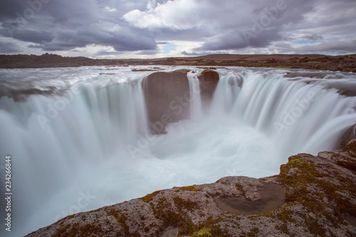 The Hrafnabjargarfoss Waterfall with golden clouds in the sky. The flowing water is captured by a long exposure. Amazing blue color of water from the glacier. Natural and colorful environment.