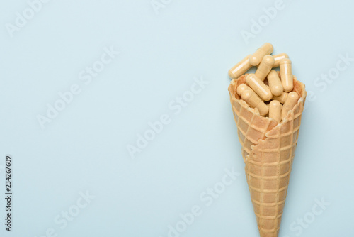 Pills in ice cream waffer cone medicine concept on blue background with copy space