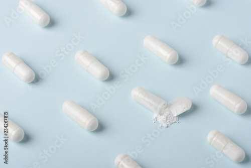 Fotografia Pills pattern with one capsule open and white powder spilling over blue backgrou