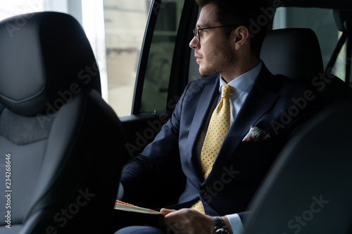 Fotografia Young businessman sitting on back seat of the car, while his chauffeur is driving automobile