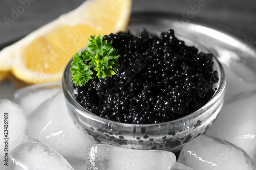 Bowl with delicious black caviar and ice-cubes, closeup photo