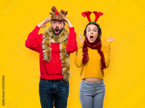 Couple dressed up for the christmas holidays with surprise and shocked facial expression on yellow background