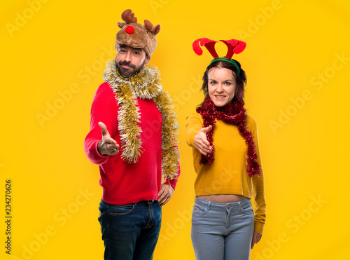 Couple dressed up for the christmas holidays shaking hands for closing a good deal on yellow background