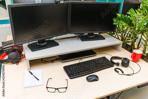 Фотография desktop in the light office on the table are two monitors, a laptop, glasses, he