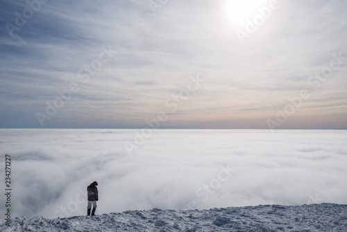 Winter hiking. Tourist on snowy mountain top enjoying beautiful view of cloudscape.