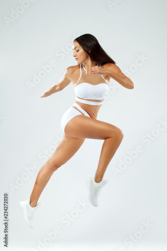 Sporty fit woman, athlete runner makes fitness exercising with jumping on white background.