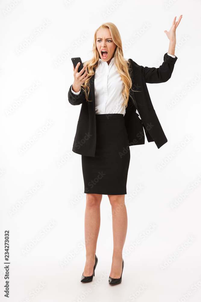Full length photo of displeased businesswoman wearing office suit screaming on smartphone, isolated over white background in studio Full length photo of displeased businesswoman wearing office suit screaming on smartphone, isolated over white background in studio