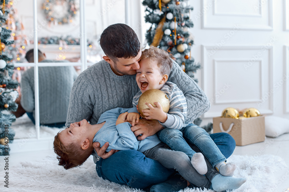 A a daddy with his two sons twins in front of the christmas tree with candles and gifts hugging and having fun. New year's eve. Cozy holiday at the fir-tree. love, happiness and big family concept A a daddy with his two sons twins in front of the christmas tree with candles and gifts hugging and having fun. New year's eve. Cozy holiday at the fir-tree. love, happiness and big family concept