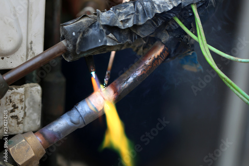 Technician are soldering a coil with copper in order to fix leakage of air compressor. This is a oil and piping problem of air-conditioner unit.