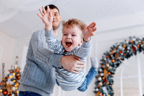 A daddy with his two sons twins in front of the christmas tree  with candles and gifts hugging and having fun. New year's eve. Cozy holiday at the fir-tree. love, happiness and big family concept