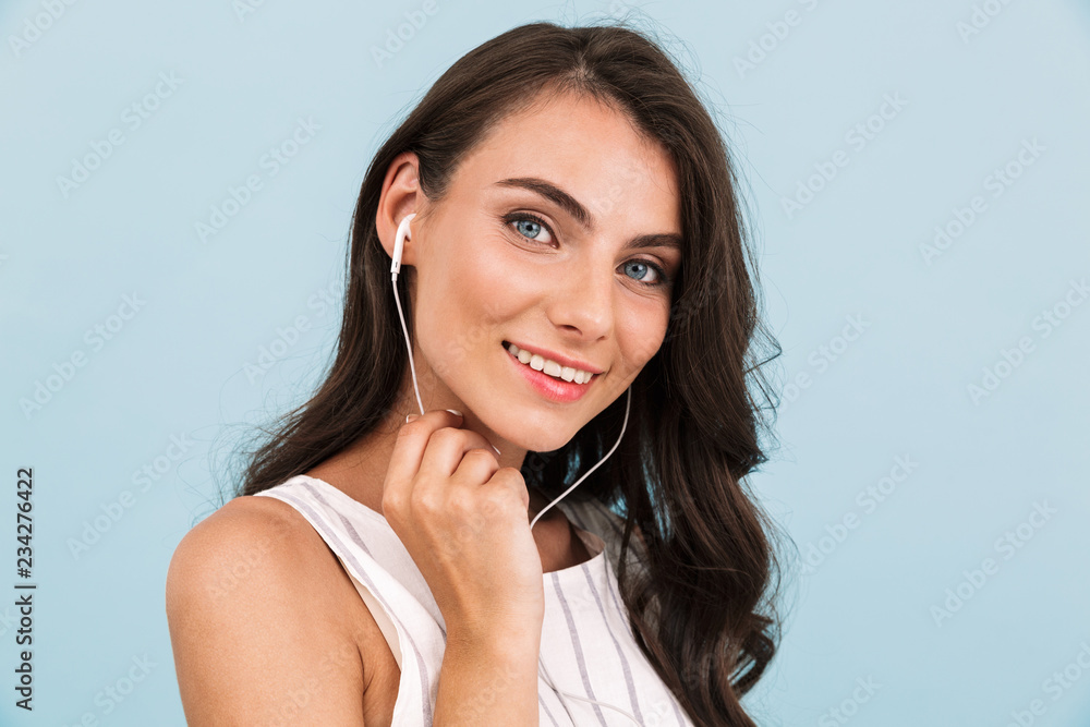 Beautiful young woman isolated over blue background wall listening music with earphones.