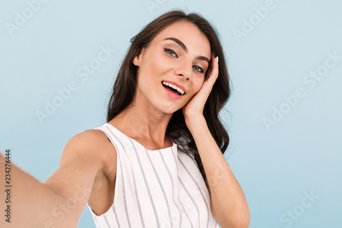 Excited young woman isolated over blue background wall make a selfie by camera.