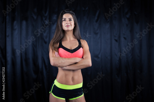 Fitness model in a pink top and sports shorts with a perfect figure posing on a dark background