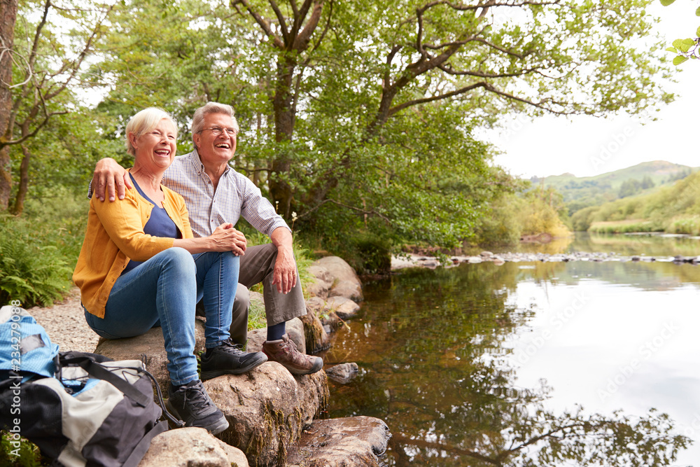 Fototapeta premium Senior Couple On Hike Sitting By River In UK Lake District