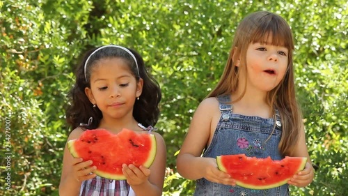 Two little girls eating a watermelon.