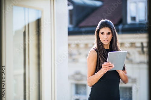 Young businesswoman with tablet standing on a terrace outside an office in city.