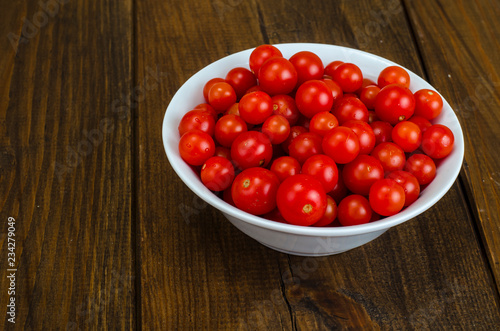 Small red cherry tomatoes in white bowl on wooden background