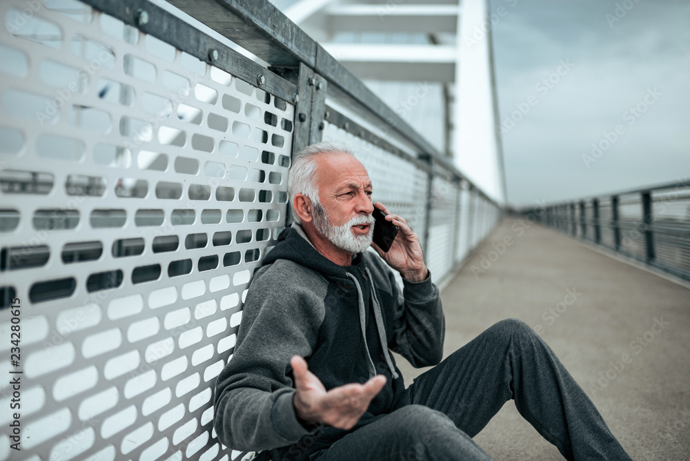 Senior man tracksuit talking on the phone while relaxing after workout. Senior man tracksuit talking on the phone while relaxing after workout.