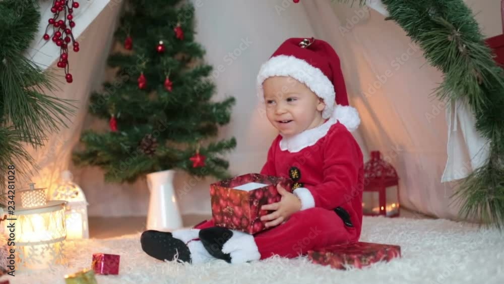 Adorable little toddler baby boy dressed in canta claus costume, playing at home in front of teepee decorated for Christmas Adorable little toddler baby boy dressed in canta claus costume, playing at home in front of teepee decorated for Christmas