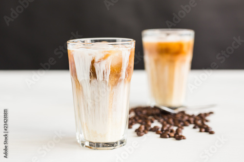 Ice coffee in a glass with cream over and coffee beans on the table