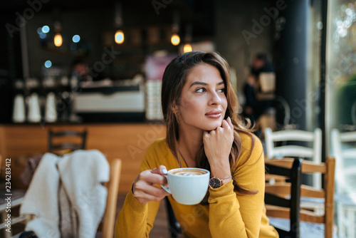 Stylish young woman drinking coffee at the cafe, looking away. photo