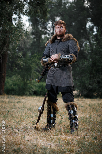 Warrior Viking in full arms with axe and shield in dark forest waiting for battle