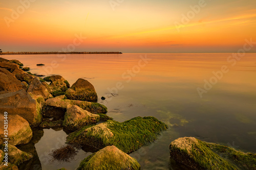 Exciting sea sunset at warm colors and colorful moss over the rocks. Smooth long exposure of waves