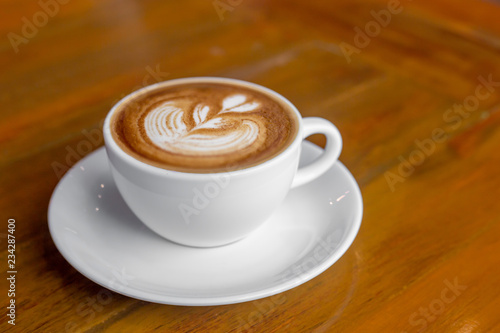 The white ceramic cup of hot capucchino coffee on the wooden table in the restaurant or coffee shop in the warm yellow light and flare. 