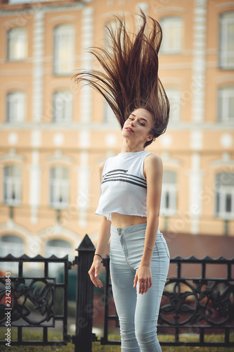 portrait of a girl in jeans and a t-shirt on the background of the building in the evening on a summer day. street dancing in the city photo