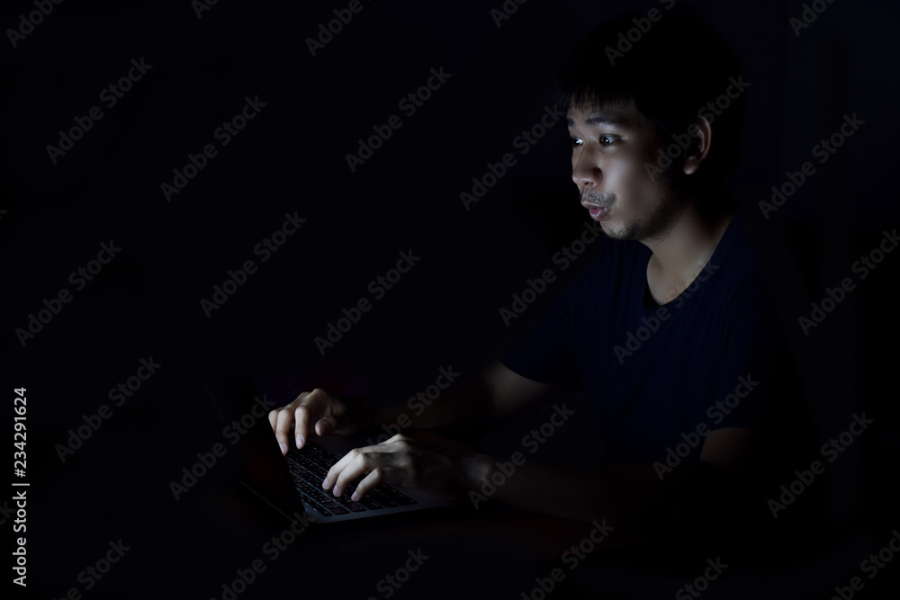 Asian man using laptop in the black dark room and show surprise something on his face