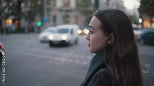 4k shot of a tired sad girl waiting to cross the street. City traffic on background. photo