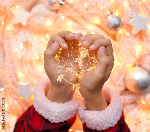 Christmas garland in the children's hands against the background of christmas lights. Holidays concept © nmelnychuk