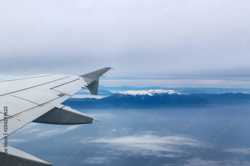 View from airplane with wing flying over Mt Olympus Greece with the snow-covered peak showing through a heavy fog View from airplane with wing flying over Mt Olympus Greece with the snow-covered peak showing through a heavy fog