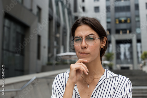 Business woman frowning her eyebrows holding index finger on chin having doubt and suspicion feeling sceptical about something. Human emotions and expressions concept. Outdoor near office building